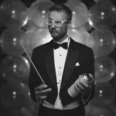 mężczyzna z batutą i farbą w spray'u z balonami w tle