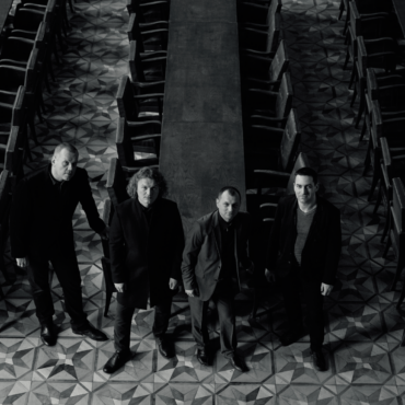 czterech mężczyzn stojących przed trzema, długimi stołami