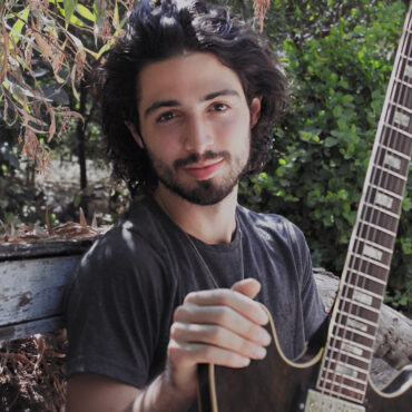 uśmiechnięty mężczyzna z gitarą, siedzący w ogrodzie